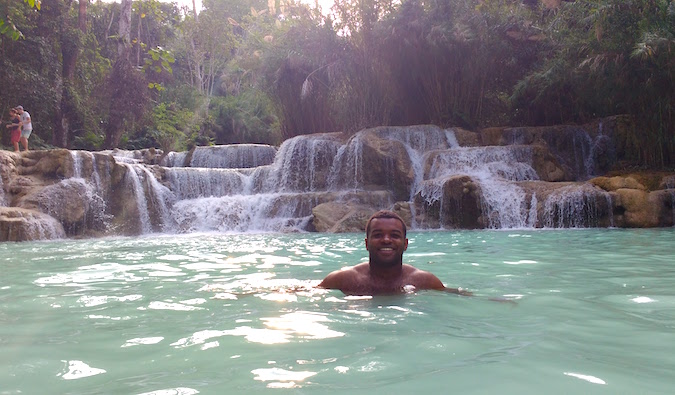 A black solo male traveler swimming in a waterfall pool in Asia