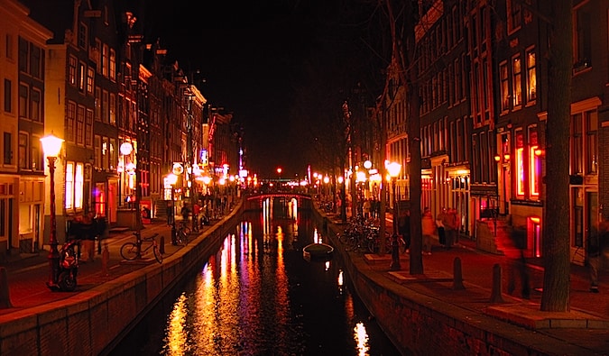 A canal going through the red light district in Amsterdam, lit up with red lights at night.