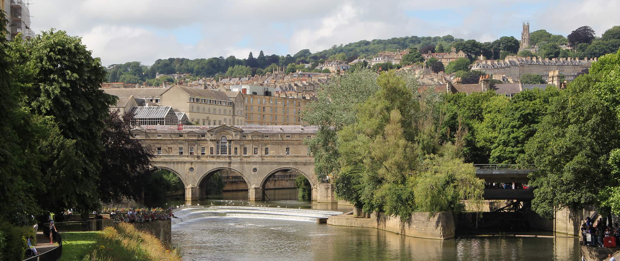 the historic bridge in Bath, England surrounded by trees on a bright summer day