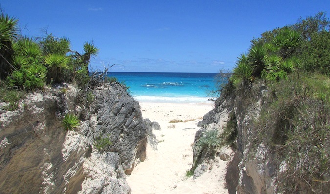 A sandy entrance on a Caribbean beach next to two large grassy rocks