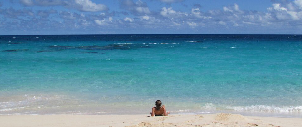 A pristine beach on the beautiful coast of Bermuda with a person resting in the shallow, clear waters
