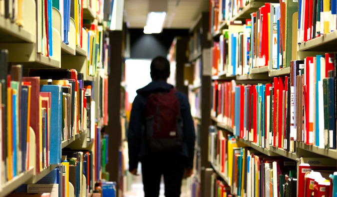 Um homem a andar numa biblioteca cheia de livros