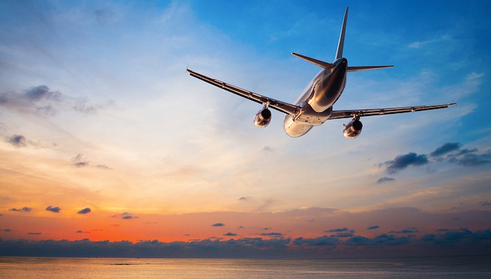 Airplane soaring over water into the sunset.