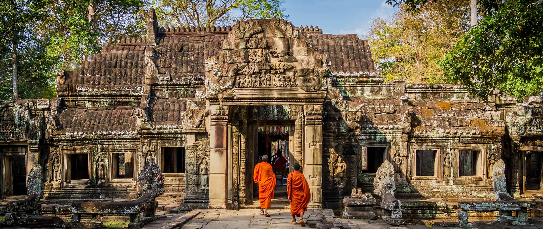 a view of Cambodia's Angkor Wat temple, with two monks in orange robes walking inside