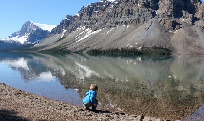 Little boy bends down to touch the beautiful lake overseas