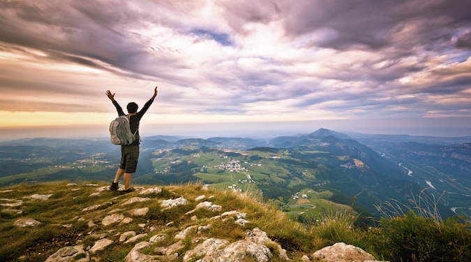 Nomadic backpacking hiker standing at the top of a mountain excited