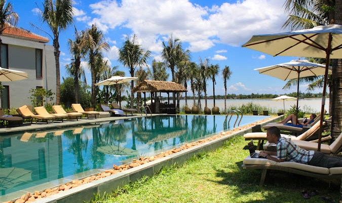 Man on his laptop on a lounge chair at a pool in overseas paradise