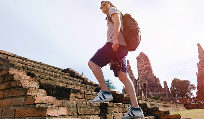 A male budget traveler walking up the steps of an ancient temple in Asia