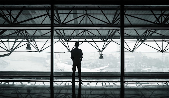 A black and white photo of a solo traveler standing alone in an airport