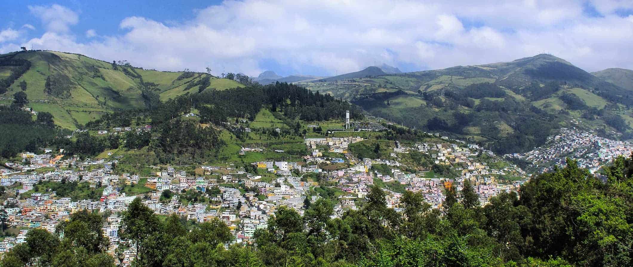 an aerial view of Quito, Ecuador surrounded by green hills on a sunny summer day