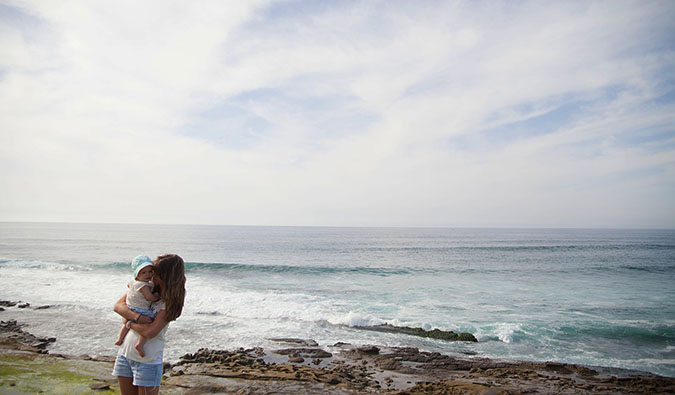 A woman holding her baby standing near the ocean