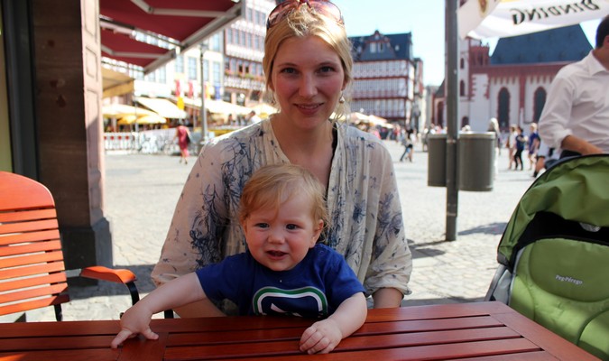 Mom and her toddler sitting at a red picnic table outside in Europe