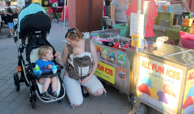 A mom carrying her newborn while feeding a toddler sitting in a stroller