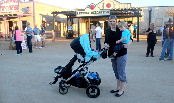 A mom carrying her child while pushing a large stroller