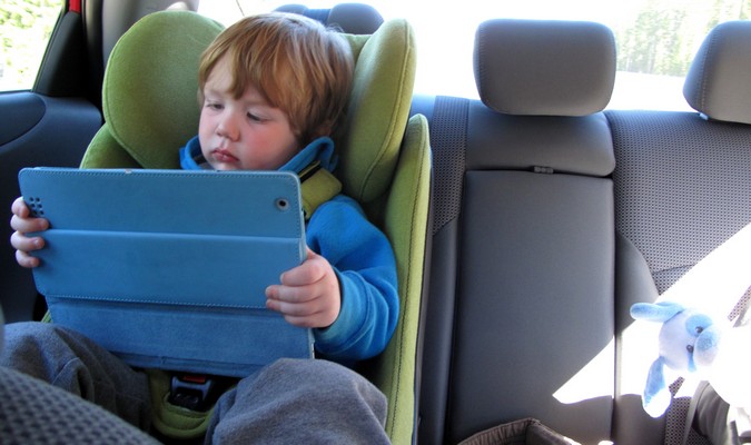 Toddler playing with electronics in the backseat on a family road trip