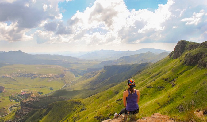 Solo traveler Kristin Addis sitting on a mountain top looking down at the view