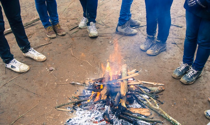 A bunch of solo travelers stand around a campfire