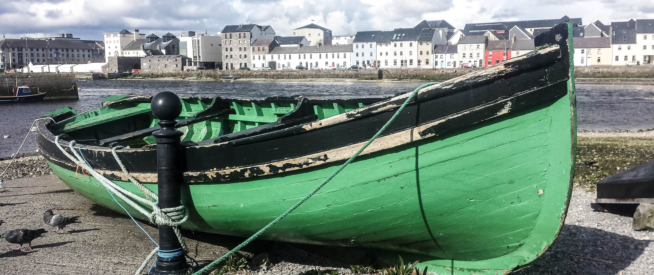 view of Galway's waterfront with a small, green boat beached in the sand along the coast