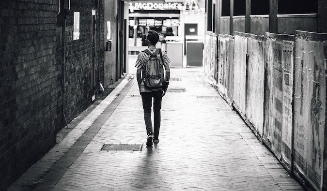 Black and white lonely solo backpacker walking through city street sadly