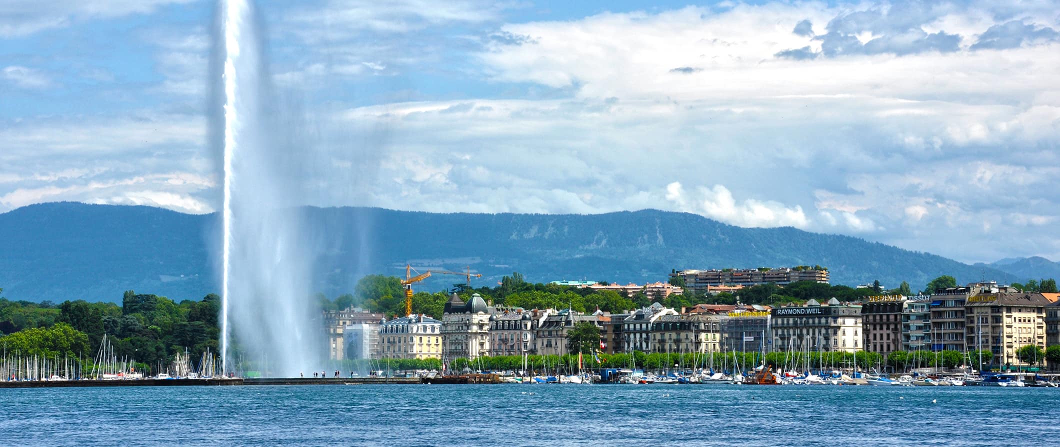 View of the jet fountain and the waterfront in Geneva, Switzerland on a bright and sunny summer day with mountains in the distance