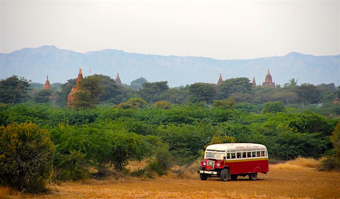 An old bus in thick foliage behind temples in Asia