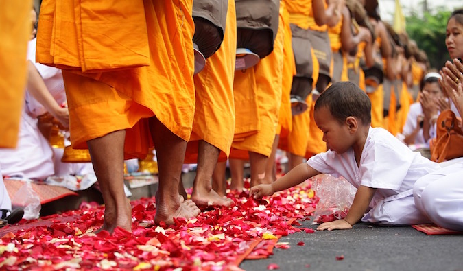 A child touching a bunch of rose petals that are laying at monks' feet