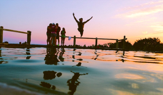 A group of travelers having fun jumping into water at sunset