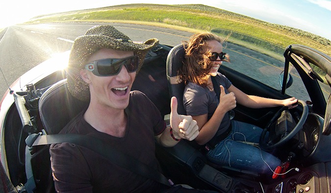 Male hitchhiker with a female driver riding along the road in a top-down convertible