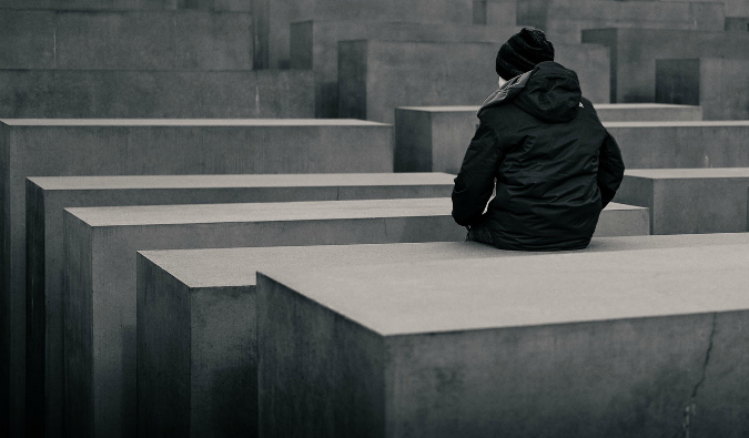 A person sitting on one of the concrete pillars of the Memorial to the Murdered Jews of Europe in Berlin, Germany