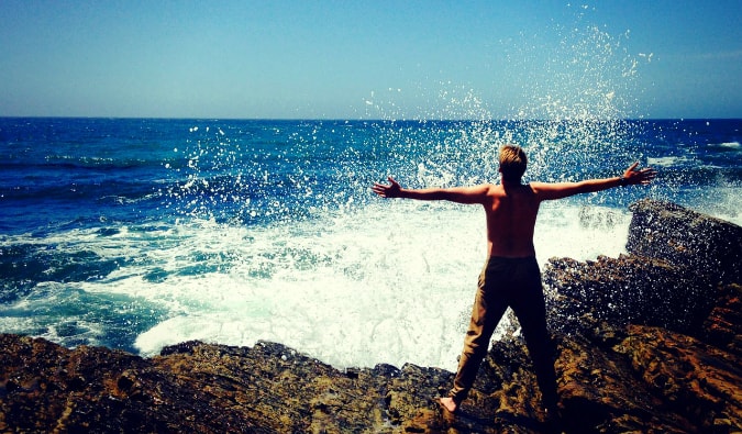 A man standing on rocks near the coast as the waves crash