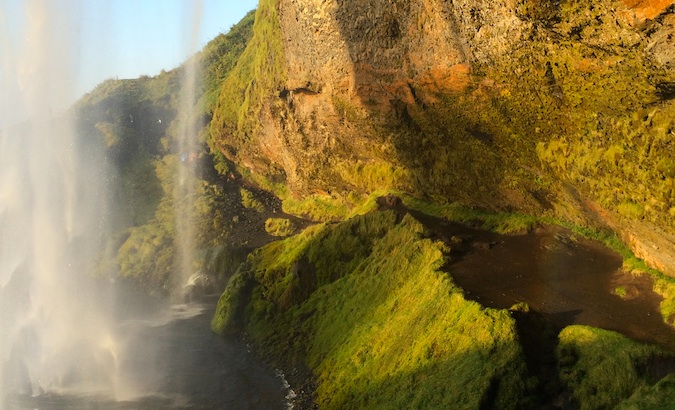 backside of Seljalandsfoss with excellent light, water, blue sky, and greenery