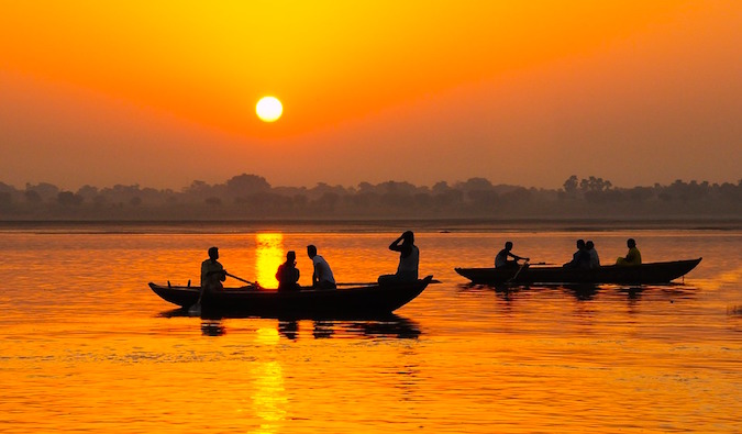 A golden sunset near a river with small fishing boats in India