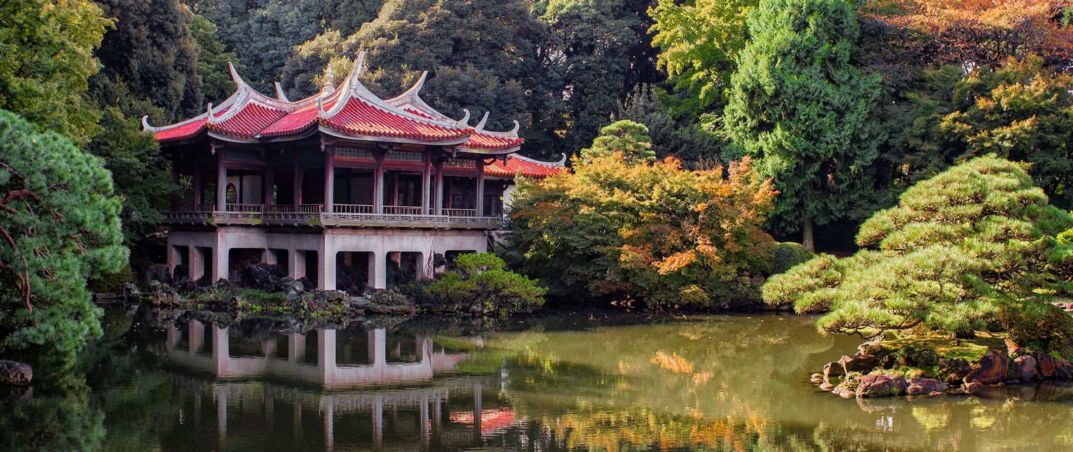 an old temple in Japan surrounded by lush trees near a small lake