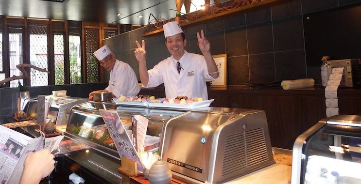 A Japanese sushi chef posing for a friendly photo from behind the counter