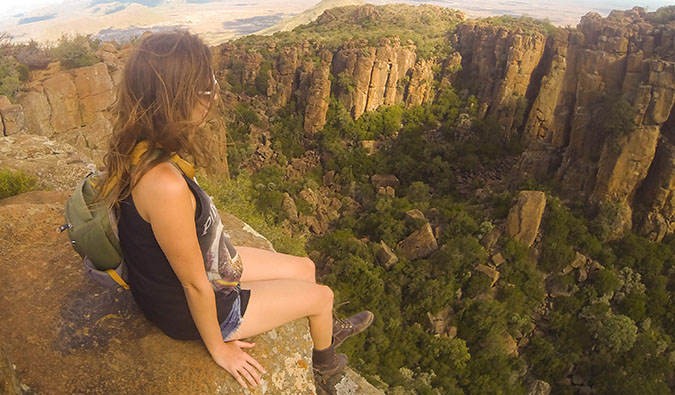 A nomadic solo female backpacker sitting on a cliff, taking in the view