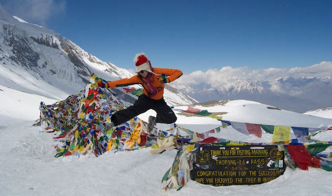 Solo female traveler jumping in from of the sign at the top of a snowy mountain