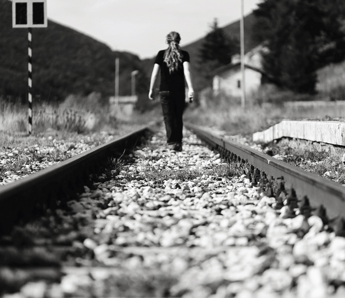 Black and white self-portrait of Laurence walking on railway tracks