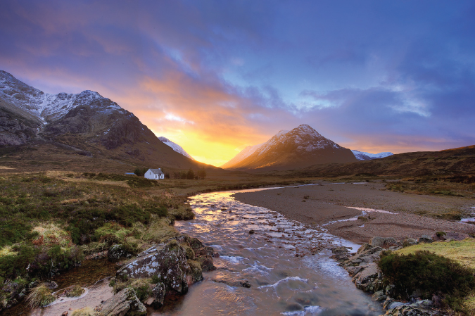 Photo of the sunsetting behind mountains in Glencoe, Scotland with a house in the midground