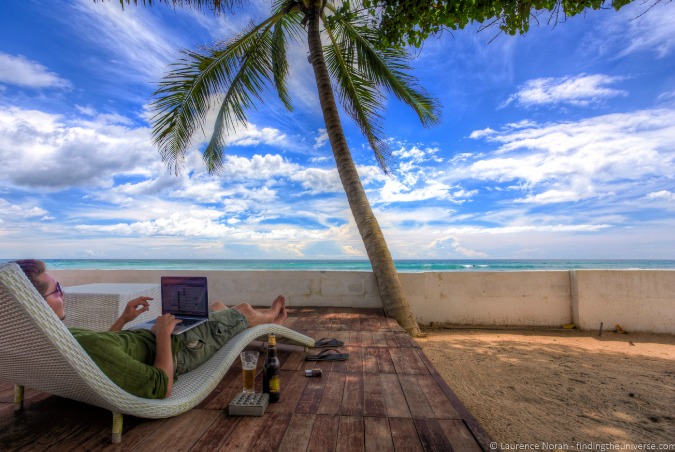 Remote worker working on a laptop beside a palm tree on a beach