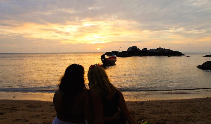 Two women together on beach overseas at sunset