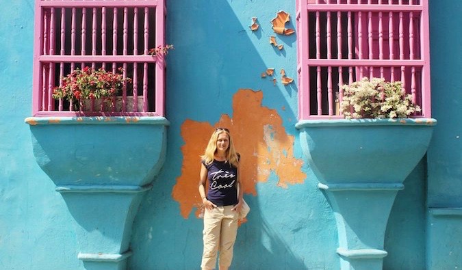 Solo lesbian traveler posing near a colorful wall aborad