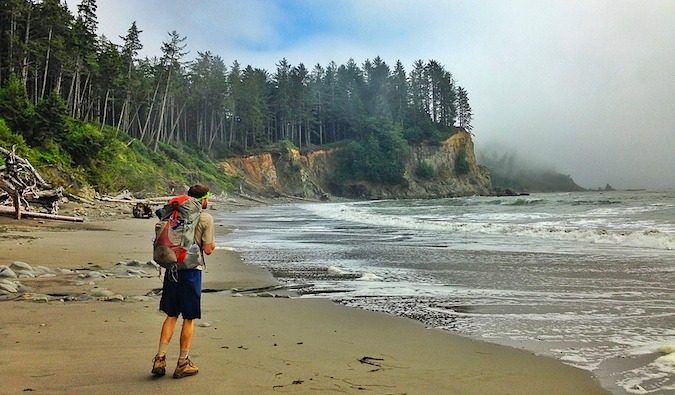 a backpacker hiking on a secluded beach surrounded by trees