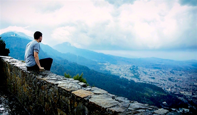 A man sitting on a wall gazing out on city on a cloudy day