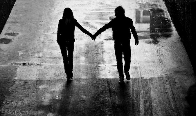 A black and white photo of a couple holding hands while walking at night