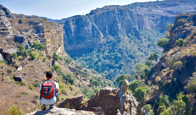 Nomadic Matt crouching on a cliff, looking in the distance over the hills and cliffs