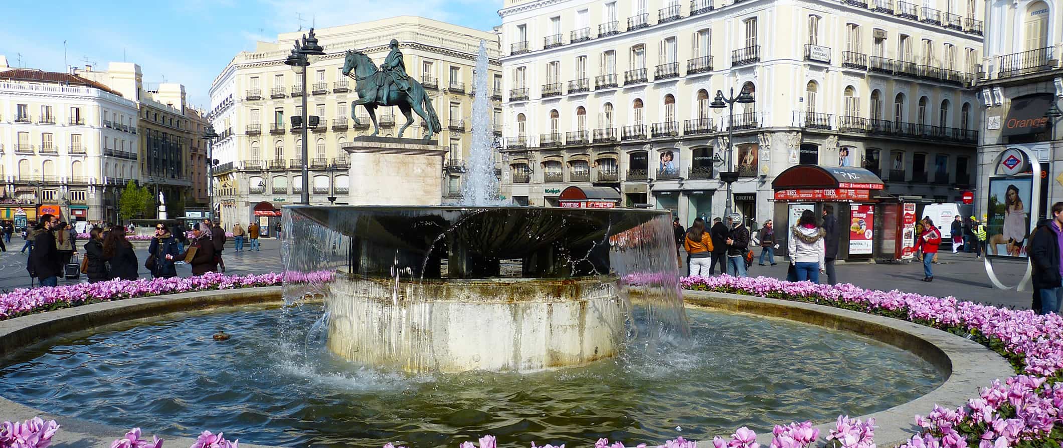 People milling around a huge, historic fountain on a sunny day in Madrid, Spain