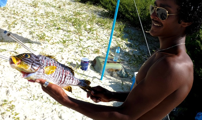 Maldivian man wearing sunglasses holding a large, freshly caught fish.