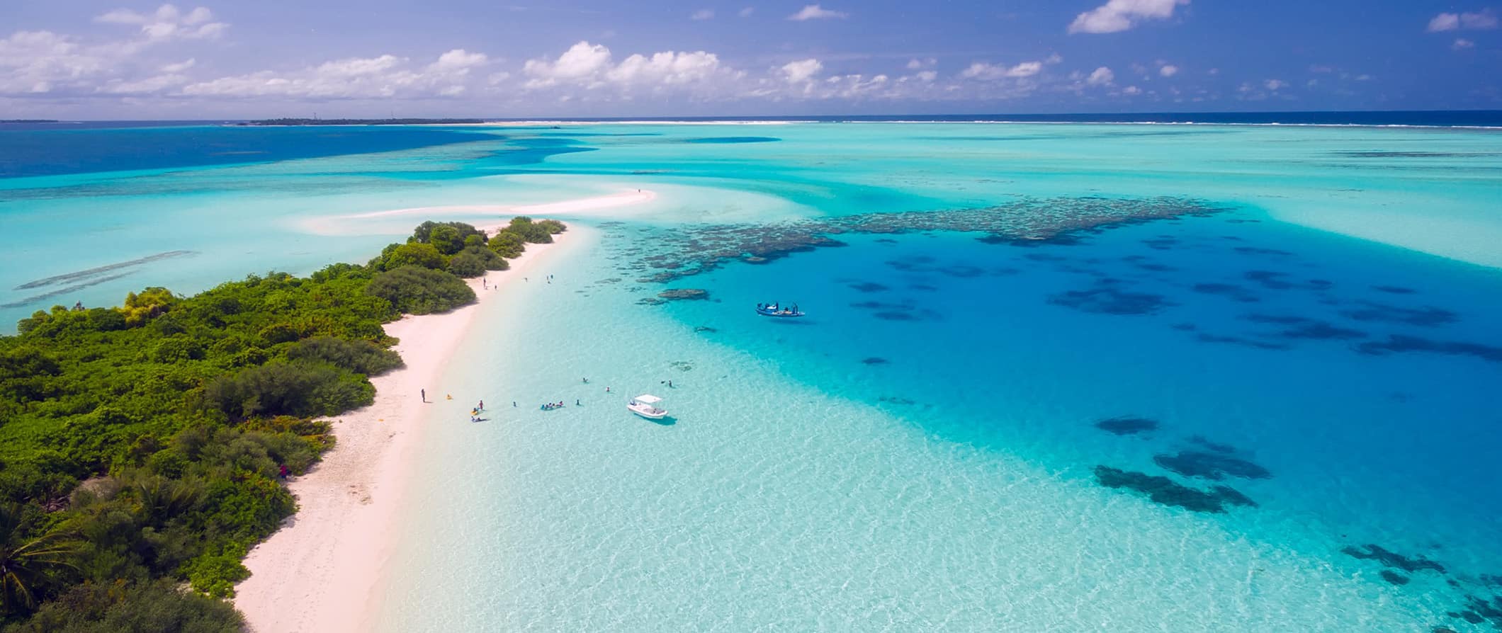 The stunning, clear tropical blues waters of the Maldives along a narrow white-sand beach