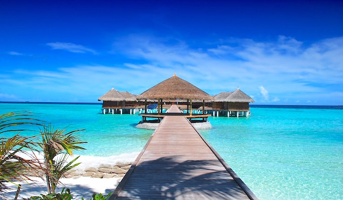 Bright turquoise waters of the Maldives with a boardwalk leading to thatched huts