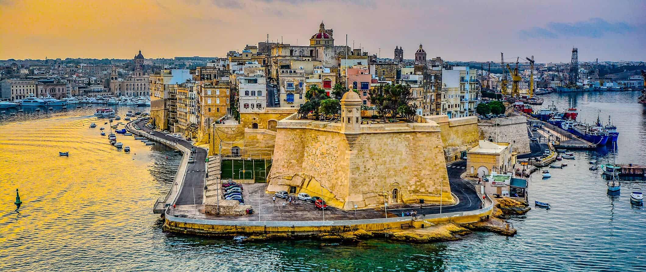 a view of the coast in Malta, lined by towering historic buildings near the harbor